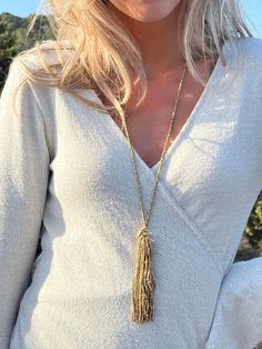 a blonde woman wearing a white top with a gold tassel on her neck and necklace