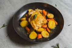 a black plate topped with chicken, potatoes and carrots on top of a table