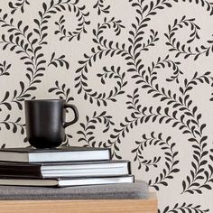 a stack of books next to a cup on top of a wooden table in front of a wall