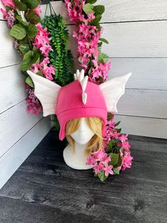 a white mannequin head wearing a pink hat with wings and flowers around it