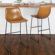 two brown leather stools sitting on top of a wooden floor next to a counter