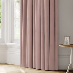 a pink curtain hanging in front of a window with white walls and wooden flooring