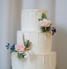 a three tiered white cake with pink flowers on the top and blue berries on the bottom