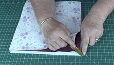 an older woman cutting fabric with a pair of scissors on top of a table next to a green mat