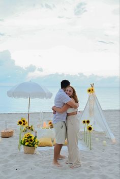 a man and woman hug on the beach with sunflowers in front of them