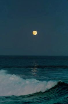 a full moon is seen over the ocean with waves in the foreground and dark blue sky