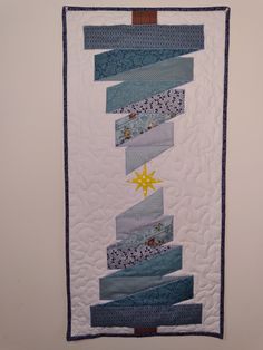 a quilted wall hanging on the side of a wall with blue and white strips