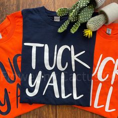 two t - shirts with the words tuck y'all on them next to a cactus