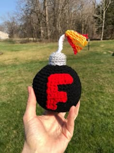 a hand is holding up a crocheted object with the letter f on it