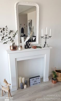 a white fireplace mantle with candles, mirror and other items on it in a living room