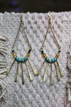 Hanging flat cable chain beaded arch with brass fringe detail. Beaded Dangle Earrings In Brass, Beaded Brass Dangle Earrings, Gold Beaded Earrings With Beaded Chain For Festival, Gold Beaded Chain Earrings For Festival, Metal Beaded Chain Dangle Earrings, Turquoise Beaded Brass Earrings, Brass Dangling Beads Earrings For Festivals, Brass Earrings With Dangling Beads For Festivals, Festival Brass Earrings With Dangling Beads