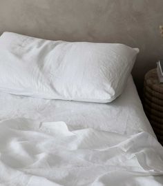 an unmade bed with white sheets and pillows on top of it, next to a wicker basket