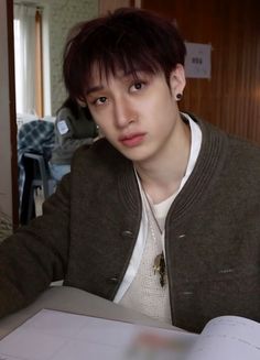 a young man sitting at a table with an open book in front of his face