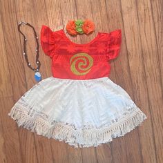 a red top and white skirt with flowers on it sitting on a wooden floor next to a necklace