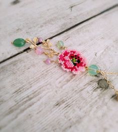 a pink flower is attached to a chain on a wooden surface with beads and charms