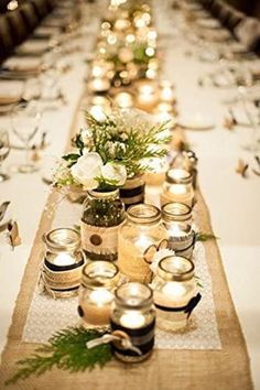 a long table is set with candles and flowers in mason jars on the runner line