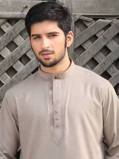 a man standing in front of a wooden fence wearing a brown shirt and black pants