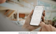 Caucasian man using smart home application on his phone to control devices at his home. Daytime shot, furnished house interior in the background. Fictional application Furnished House, Smart Home, House Interior