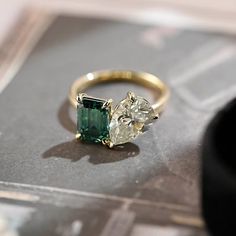 an emerald and diamond ring sitting on top of a table