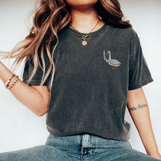 "🦢💕 Add a playful twist to your daily look with our \"Silly Goose\" Embroidered T-Shirt! This charming shirt brings a splash of whimsy to your outfit, featuring a uniquely embroidered goose that's not just silly but ready to take on the world. Crafted with attention to detail, this Embroidered Shirt showcases a goose in a stance that's both playful and assertively fun. Made from high-quality materials, our T-Shirt offers both comfort and durability, ensuring you can enjoy wearing it time and time again. Whether you're drawn to Simple Embroidery or in search of a piece that showcases your love for fun and humor with a Funny Goose Shirt, this \"Silly Goose\" T-Shirt is the perfect pick. Don't just wear any shirt; choose one that reflects your quirky personality and love for all things ligh Everyday Embroidered Tops With Relaxed Fit, Relaxed Fit Embroidered Tops For Everyday, Everyday Relaxed Fit Embroidered Tops, Trendy Embroidered Relaxed Fit Tops, Everyday Crew Neck Tops With Embroidered Graphics, Crew Neck Top With Embroidered Graphics For Everyday, Casual Everyday Tops With Embroidered Text, Casual Tops With Embroidered Text For Everyday, Casual Shirt With Embroidered Graphics And Relaxed Fit