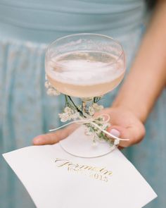 a close up of a person holding a wine glass with flowers in it and a card