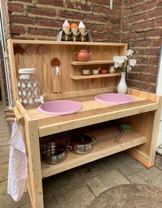 a wooden play kitchen with pink bowls on the top and shelves above it, outside