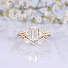 an emerald cut diamond engagement ring with side stones in yellow gold setting on a white background