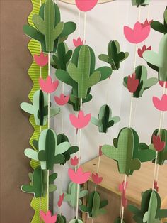 a group of paper cactus hanging from strings on a wall next to a wooden table