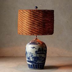 a blue and white table lamp with a woven shade on it's base, next to a wall