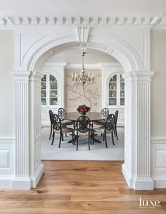 an archway leads to a formal dining room with white walls and wood flooring, along with a chandelier hanging from the ceiling