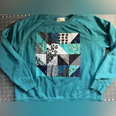 A Thrifted Crewneck Sweater, In Teal, Size Xlarge. Custom Made Quilt Square On The Center Front Of Jumper. Various Fun Fabrics, And One Featuring A Cute Cat! Stand Out In Style, In A Sustainable And Unique Way! Measurements In Photos: Total Length 23.5 Inches, Pit To Pit 24 Inches. Diy Quilted Sweatshirt, Quilt Applique Sweatshirt, Thrifted Crewneck, Cat Stand, Fur Lined Hoodie, Quilted Sweater, Fuzzy Hoodie, Stitch Hoodie, Applique Sweatshirt