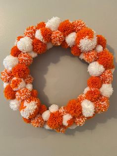 an orange and white pom - pom wreath hanging on the wall in front of a gray wall