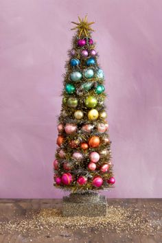 a small christmas tree with ornaments on it in front of a purple wall and wooden floor