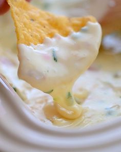 a hand holding a tortilla chip over a bowl of dip