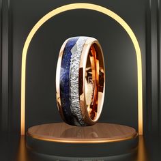 two wedding bands with blue and gold inlays are displayed on a wooden stand