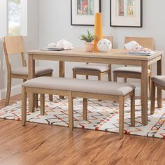 a dining room table with four chairs and a bench in front of it on a rug