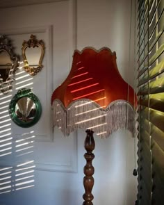 a red lamp sitting on top of a wooden table next to a mirror and shutters