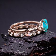 two gold rings with opal and diamonds on top of each other, sitting on a rock