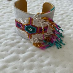 a white bracelet with colorful beads and tassels sitting on top of a bed