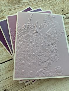 four cards with white embossing on them sitting on top of a wooden table