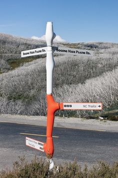 an orange and white street sign sitting on the side of a road next to bushes