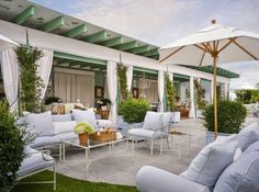 an outdoor living area with white furniture and umbrellas on the roof, surrounded by greenery