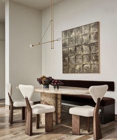 a dining room table with four chairs and a bench in front of it, next to a painting on the wall