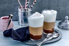 two cups filled with liquid sitting on top of a metal tray next to spoons