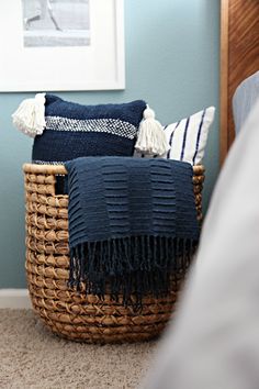 a basket with some blue and white pillows on top of it next to a bed