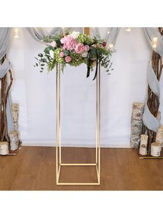 a floral arrangement on a gold stand in front of blue drapes and wooden floors