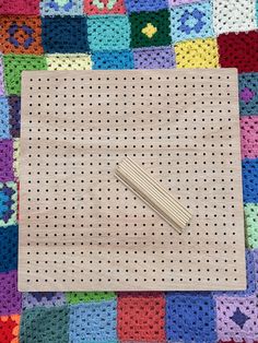 a crocheted piece of cloth with pins in it sitting on a colorful blanket