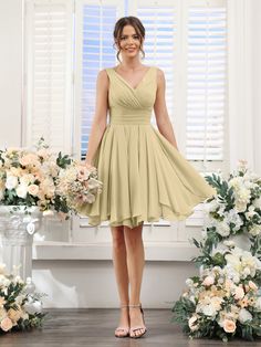 a woman standing in front of flowers wearing a short yellow bridesmaid dress and heels