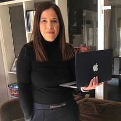 a woman standing in front of a couch holding an apple laptop