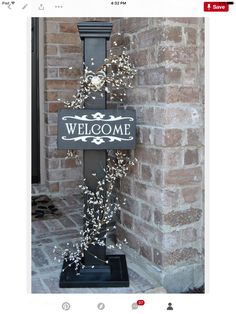 a welcome sign on the side of a brick building next to a lamp post with flowers growing out of it